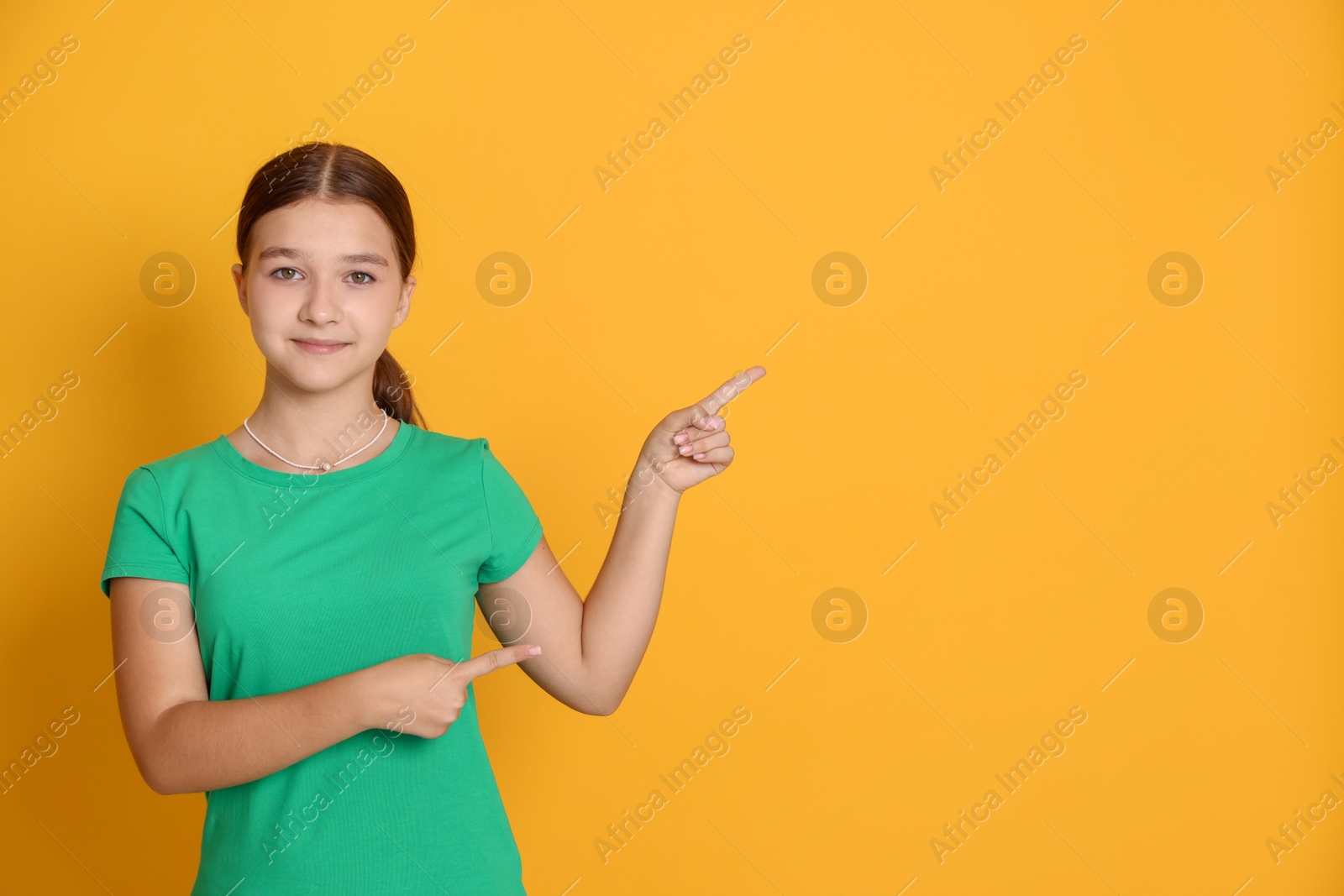 Teenage girl pointing at something on orange background, space for text Photo of Teenage girl pointing at something on orange background, space for text