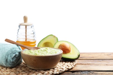 Photo of Homemade hair mask in bowl, fresh ingredients and towel on wooden table against white background. Space for text