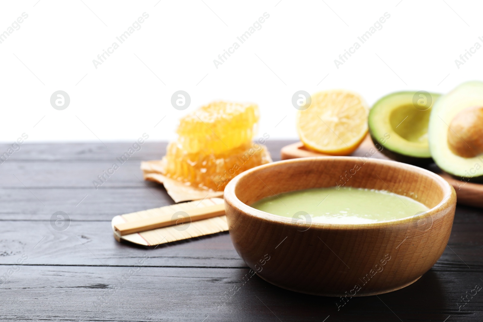 Photo of Homemade hair mask in bowl, fresh ingredients and bamboo comb on wooden table against white background. Space for text