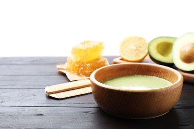 Photo of Homemade hair mask in bowl, fresh ingredients and bamboo comb on wooden table against white background. Space for text