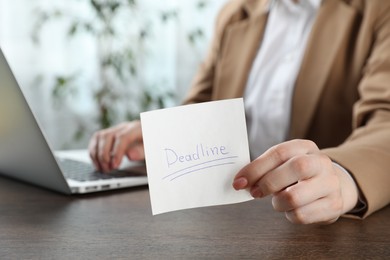 Photo of Woman holding sticky note with word Deadline at wooden table in office, closeup
