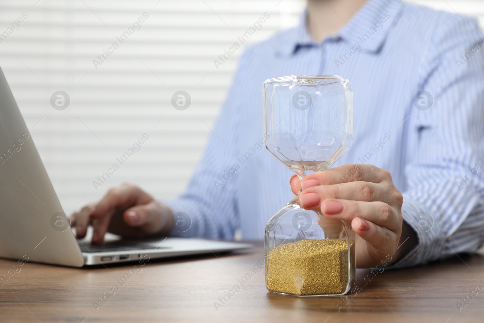 Deadline. Woman with hourglass and laptop working at wooden table in office, closeup Photo of Deadline. Woman with hourglass and laptop working at wooden table in office, closeup