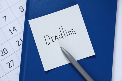 Photo of Sticky note with word Deadline, notebook, pen and calendar on table, top view