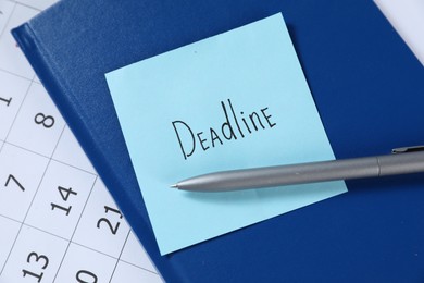 Photo of Sticky note with word Deadline, notebook, pen and calendar on table, top view