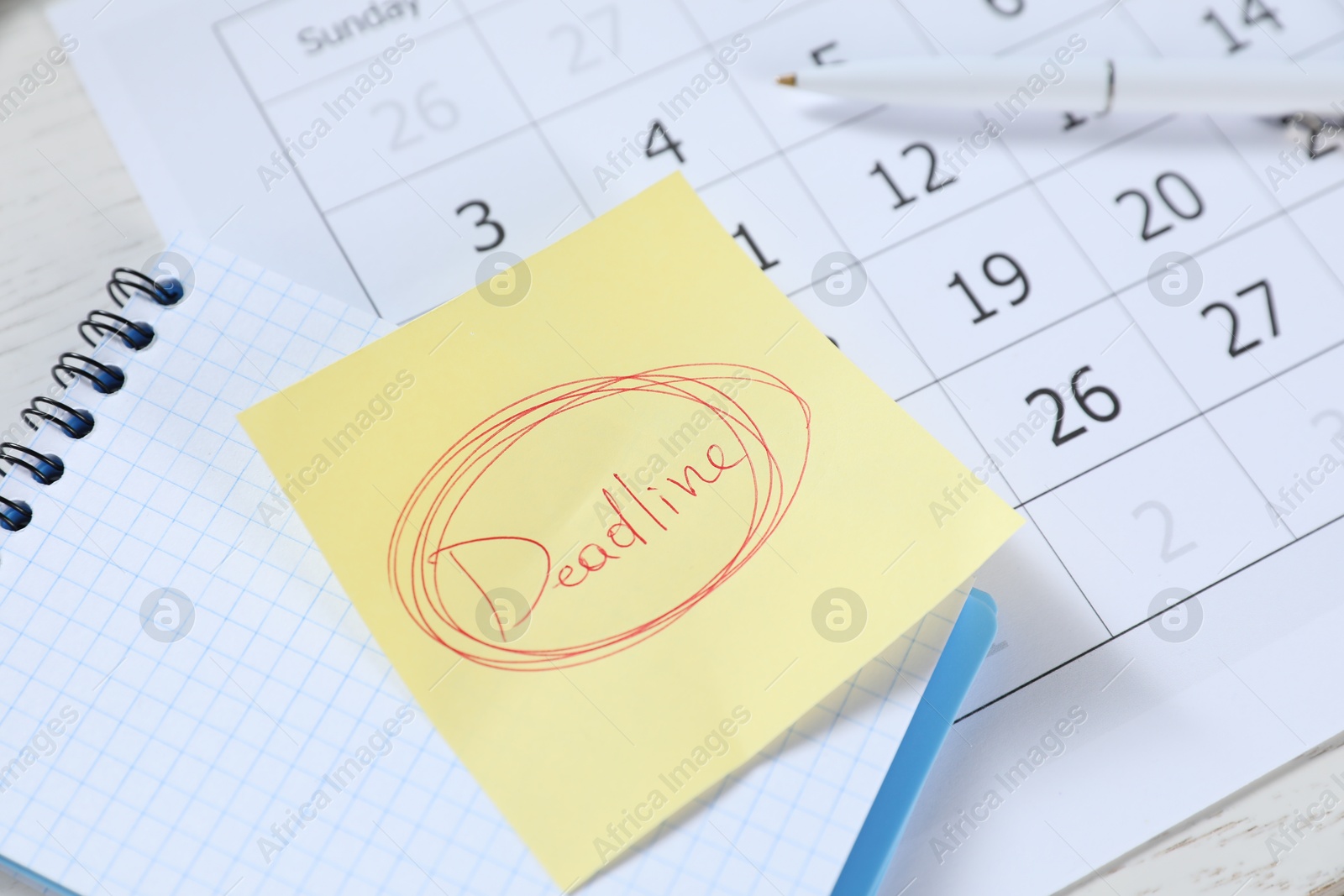 Photo of Sticky note with word Deadline, notebook, pen and calendar on table, closeup