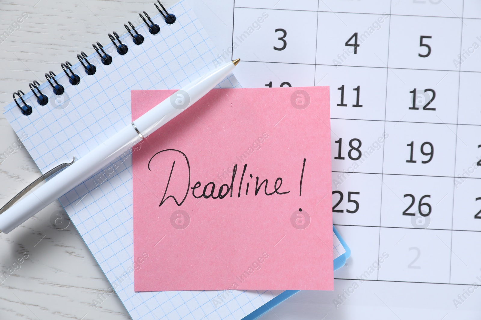 Photo of Sticky note with word Deadline, notebook, calendar and pen on white wooden table, top view