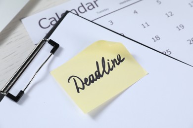 Photo of Sticky note with word Deadline, clipboard and calendar on white wooden table, closeup