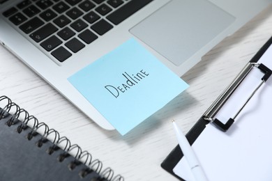 Photo of Sticky note with word Deadline, laptop, notebook, clipboard and pen on white wooden table, closeup