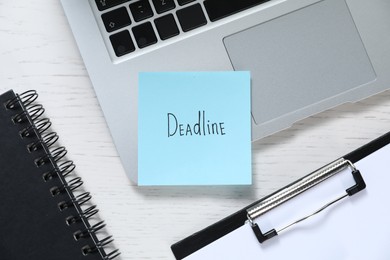 Photo of Sticky note with word Deadline, laptop, notebook and clipboard on white wooden table, flat lay