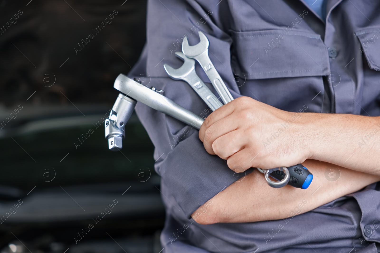 Auto parts. Professional mechanic with different wrenches near open hood of car indoors, closeup. Space for text Photo of Auto parts. Professional mechanic with different wrenches near open hood of car indoors, closeup. Space for text
