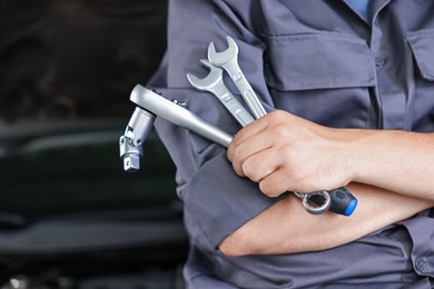Photo of Auto parts. Professional mechanic with different wrenches near open hood of car indoors, closeup. Space for text