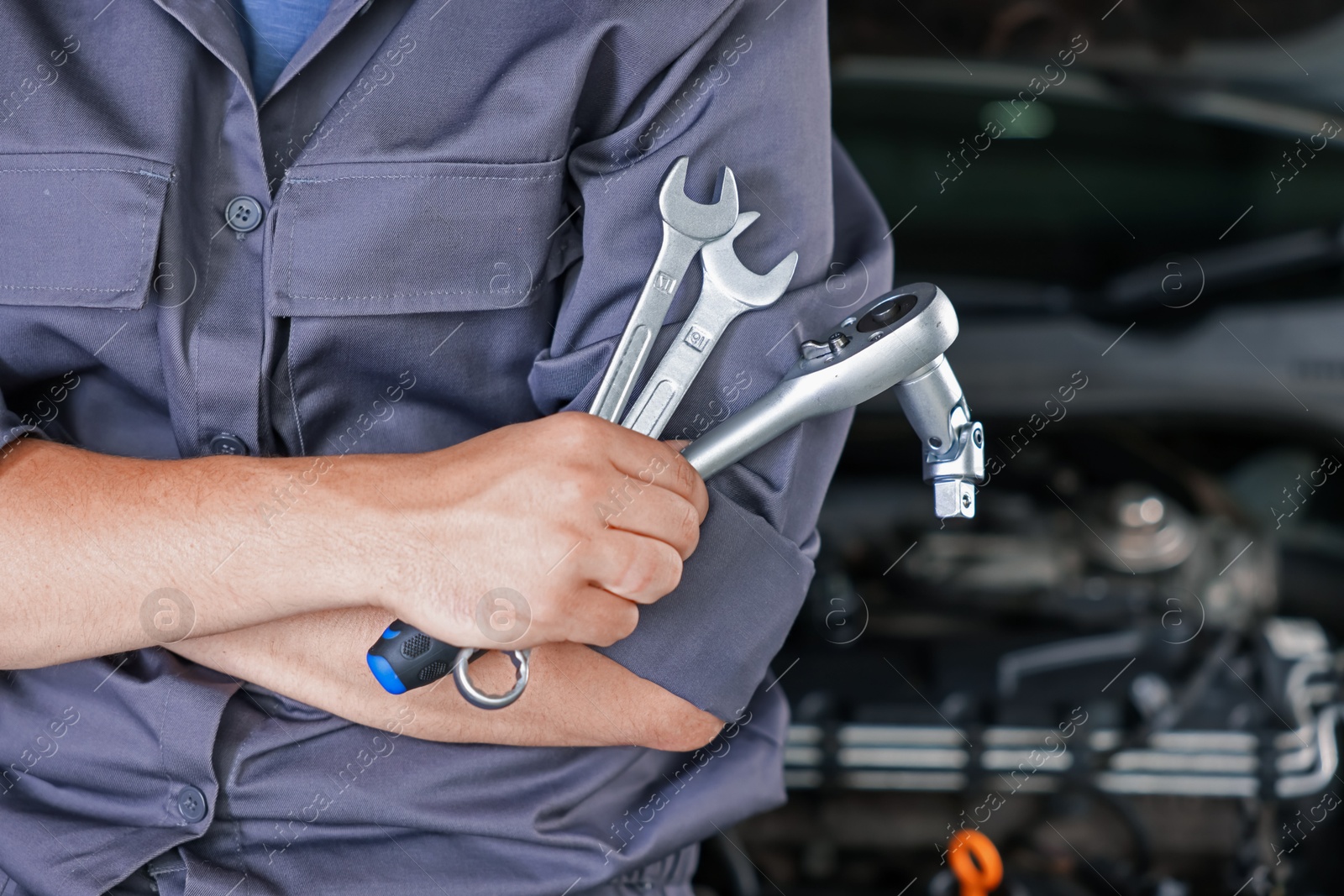 Auto parts. Professional mechanic with different wrenches near open hood of car indoors, closeup. Space for text Photo of Auto parts. Professional mechanic with different wrenches near open hood of car indoors, closeup. Space for text
