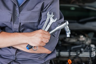 Photo of Auto parts. Professional mechanic with different wrenches near open hood of car indoors, closeup. Space for text