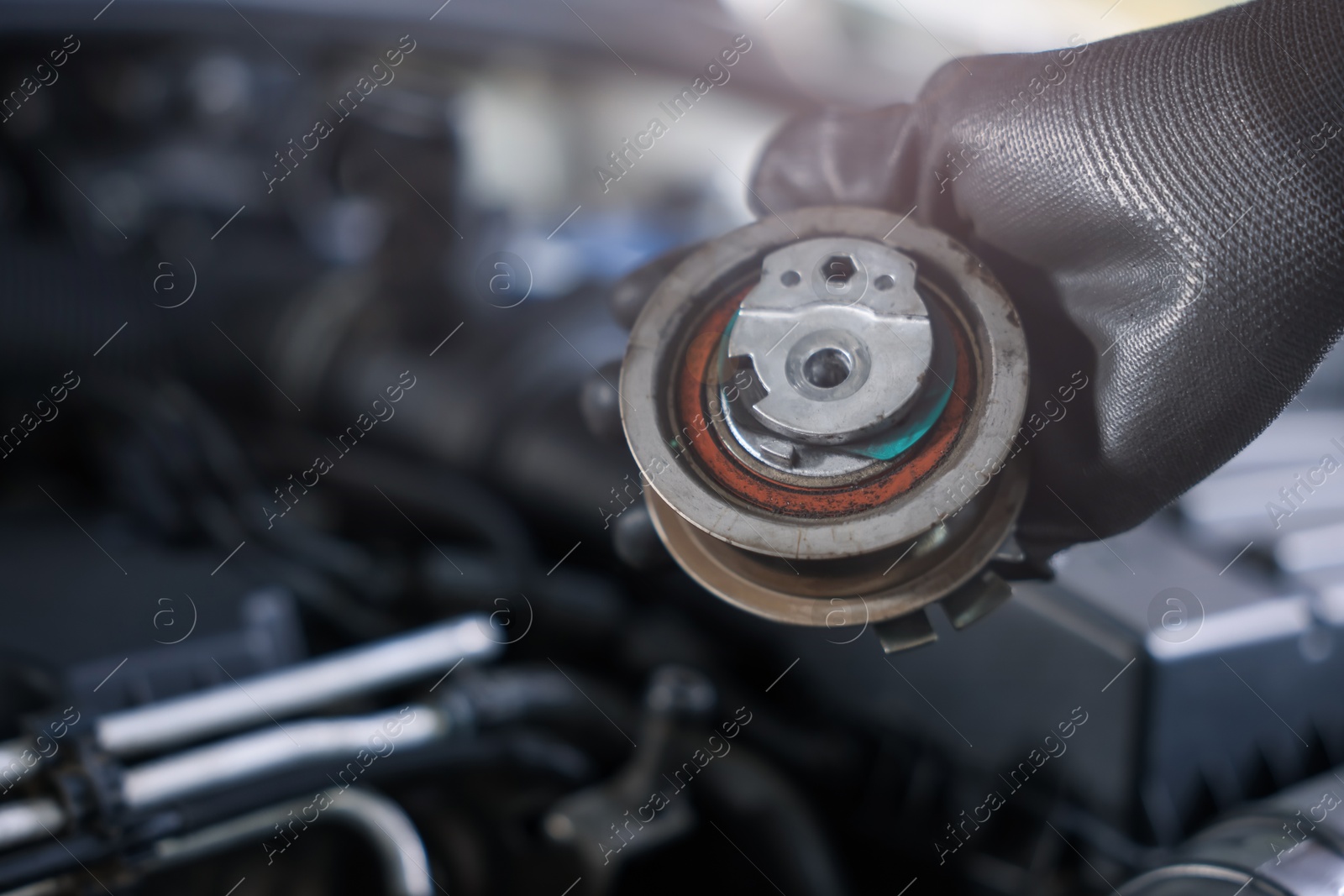 Auto part. Professional mechanic with idler-wheel near open hood of car indoors, closeup. Space for text Photo of Auto part. Professional mechanic with idler-wheel near open hood of car indoors, closeup. Space for text