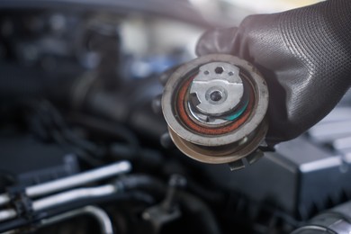 Photo of Auto part. Professional mechanic with idler-wheel near open hood of car indoors, closeup. Space for text