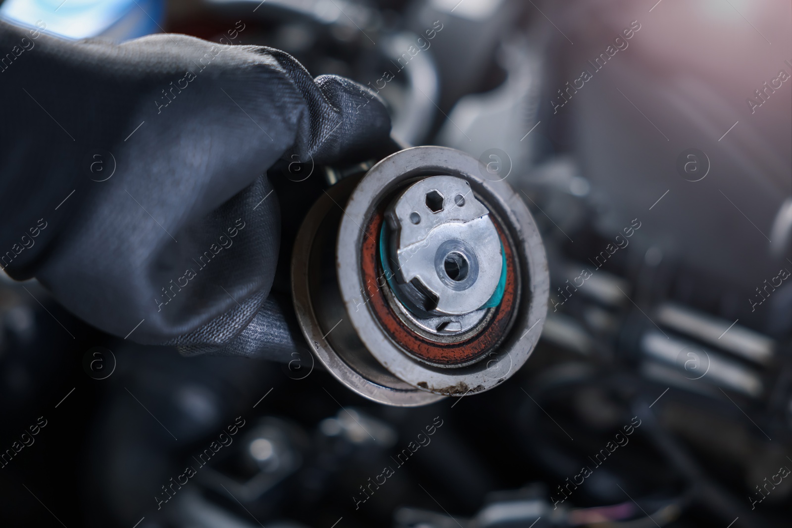 Auto part. Professional mechanic with idler-wheel near open hood of car indoors, closeup Photo of Auto part. Professional mechanic with idler-wheel near open hood of car indoors, closeup
