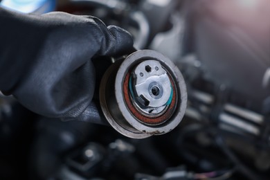 Photo of Auto part. Professional mechanic with idler-wheel near open hood of car indoors, closeup