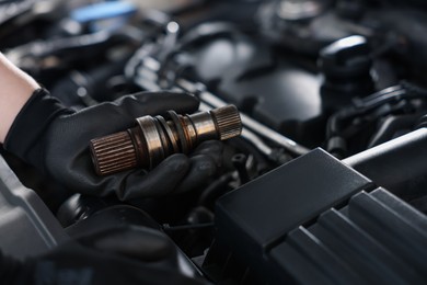 Photo of Auto part. Professional mechanic with drive shaft near open hood of car indoors, closeup