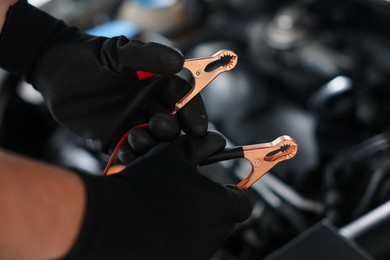 Photo of Auto part. Professional mechanic with crocodile clips near open hood of car indoors, closeup