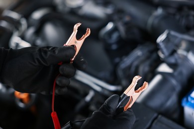 Photo of Auto part. Professional mechanic with crocodile clips near open hood of car indoors, closeup