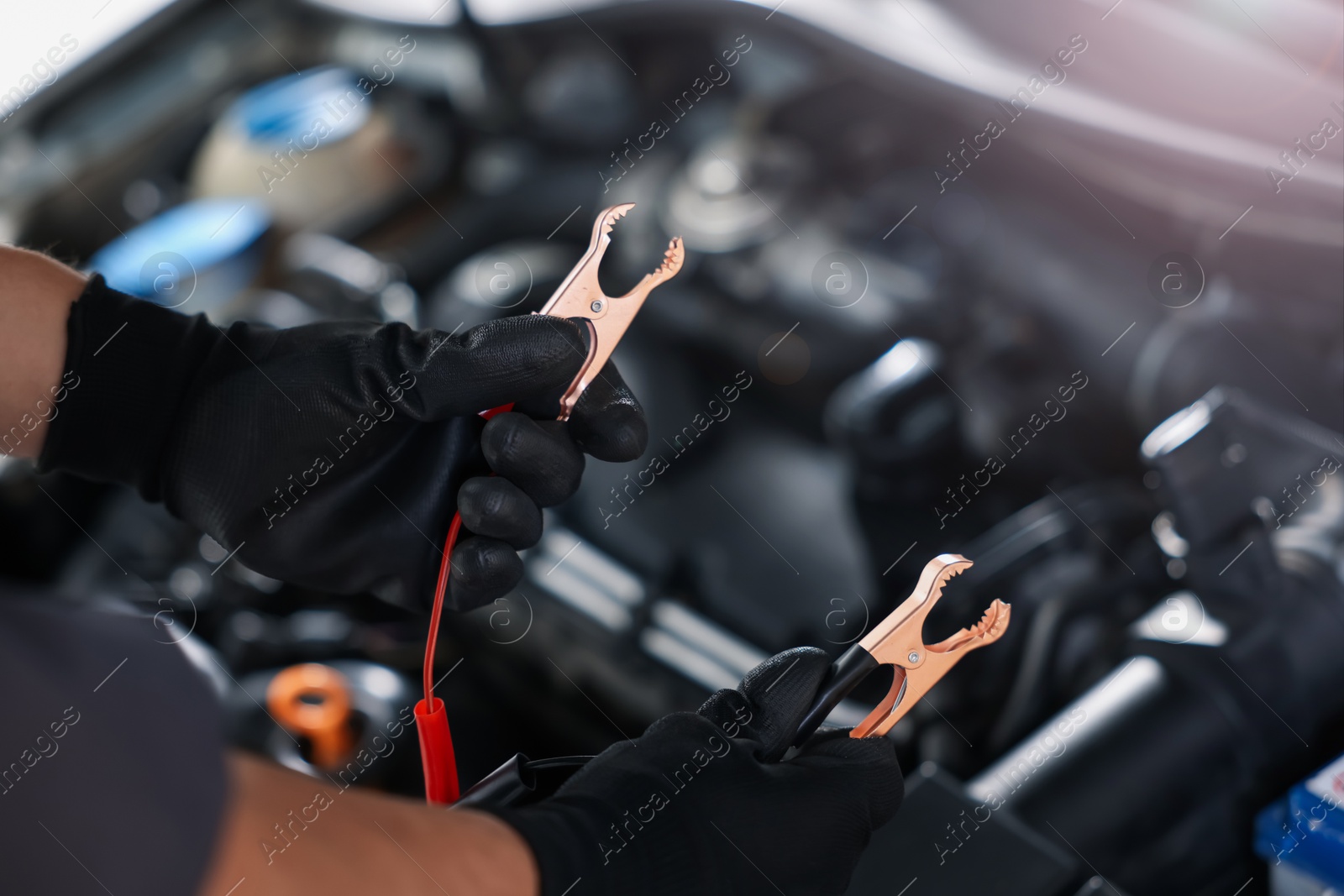 Auto part. Professional mechanic with crocodile clips near open hood of car indoors, closeup Photo of Auto part. Professional mechanic with crocodile clips near open hood of car indoors, closeup