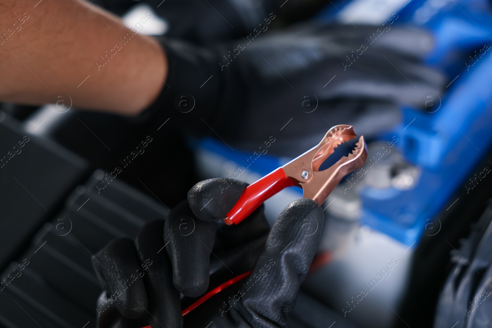 Photo of Auto part. Professional mechanic with crocodile clip near open hood of car indoors, closeup