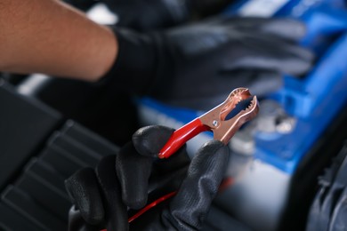 Photo of Auto part. Professional mechanic with crocodile clip near open hood of car indoors, closeup