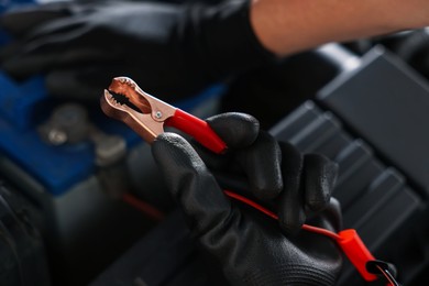 Photo of Auto part. Professional mechanic with crocodile clip near open hood of car indoors, closeup