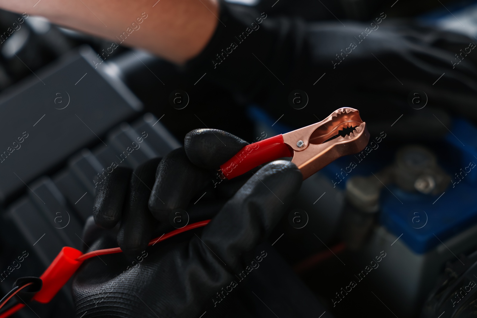 Auto part. Professional mechanic with crocodile clip near open hood of car indoors, closeup Photo of Auto part. Professional mechanic with crocodile clip near open hood of car indoors, closeup
