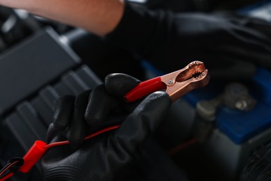 Photo of Auto part. Professional mechanic with crocodile clip near open hood of car indoors, closeup
