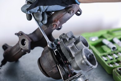 Photo of Auto parts. Professional mechanic with wrench fixing turbocharger at grey table indoors, closeup