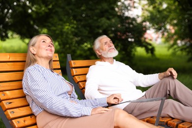 Photo of Lovely senior couple resting on wooden sunbeds in park