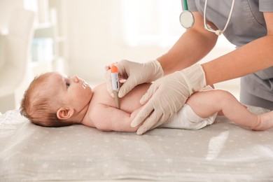 Photo of Pediatrician examining baby with thermometer at table in clinic, closeup