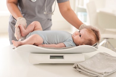 Photo of Pediatrician weighting baby with scales at white table in clinic, closeup