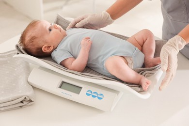 Photo of Pediatrician weighting baby with scales at white table in clinic, closeup