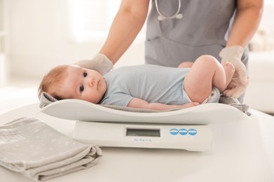 Photo of Pediatrician weighting baby with scales at white table in clinic, closeup
