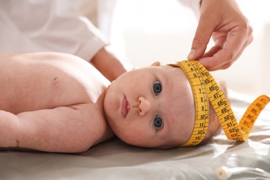 Photo of Pediatrician measuring baby's head with tape at table in clinic, closeup