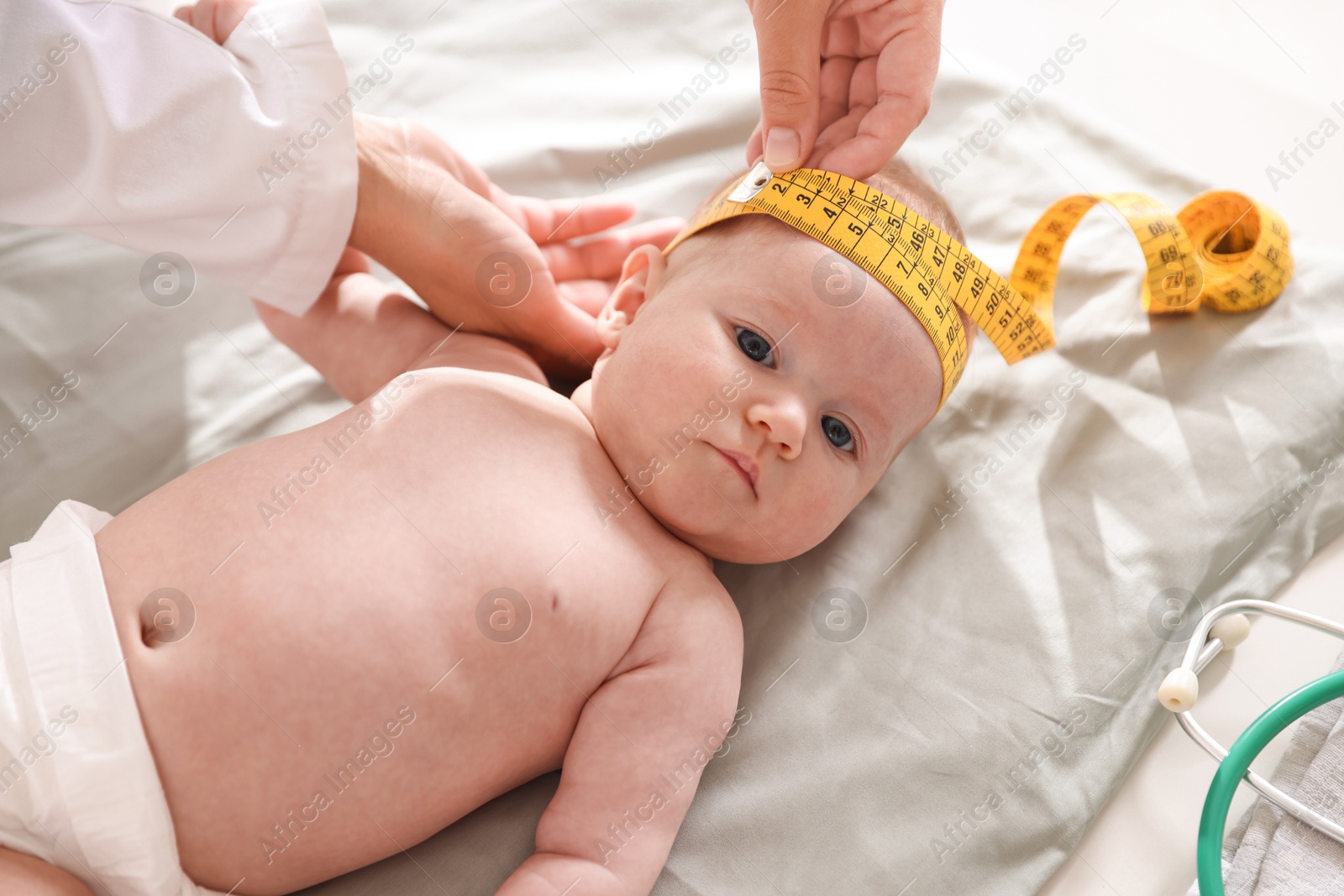 Pediatrician measuring baby's head with tape at table in clinic, closeup Photo of Pediatrician measuring baby's head with tape at table in clinic, closeup