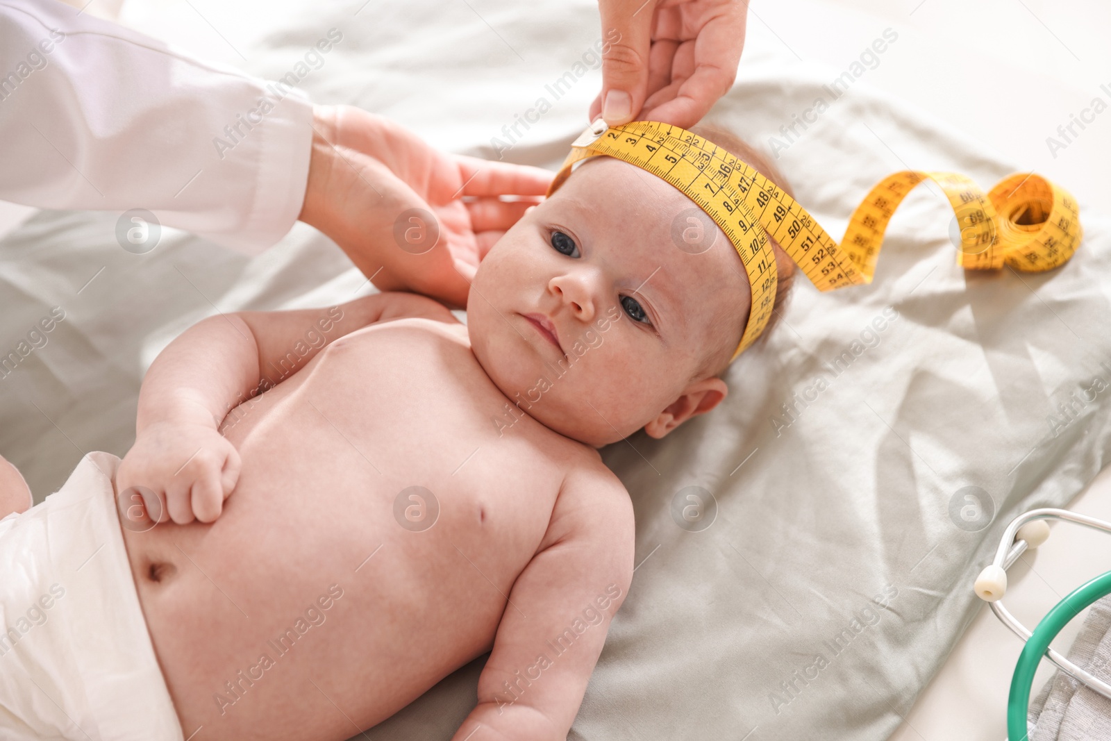 Pediatrician measuring baby's head with tape at table in clinic, closeup Photo of Pediatrician measuring baby's head with tape at table in clinic, closeup