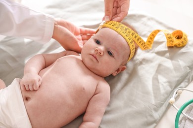Photo of Pediatrician measuring baby's head with tape at table in clinic, closeup