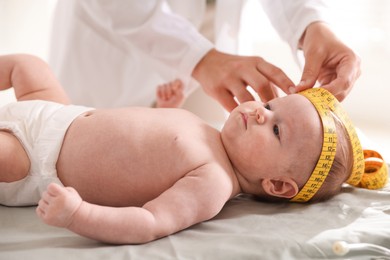 Photo of Pediatrician measuring baby's head with tape at table in clinic, closeup