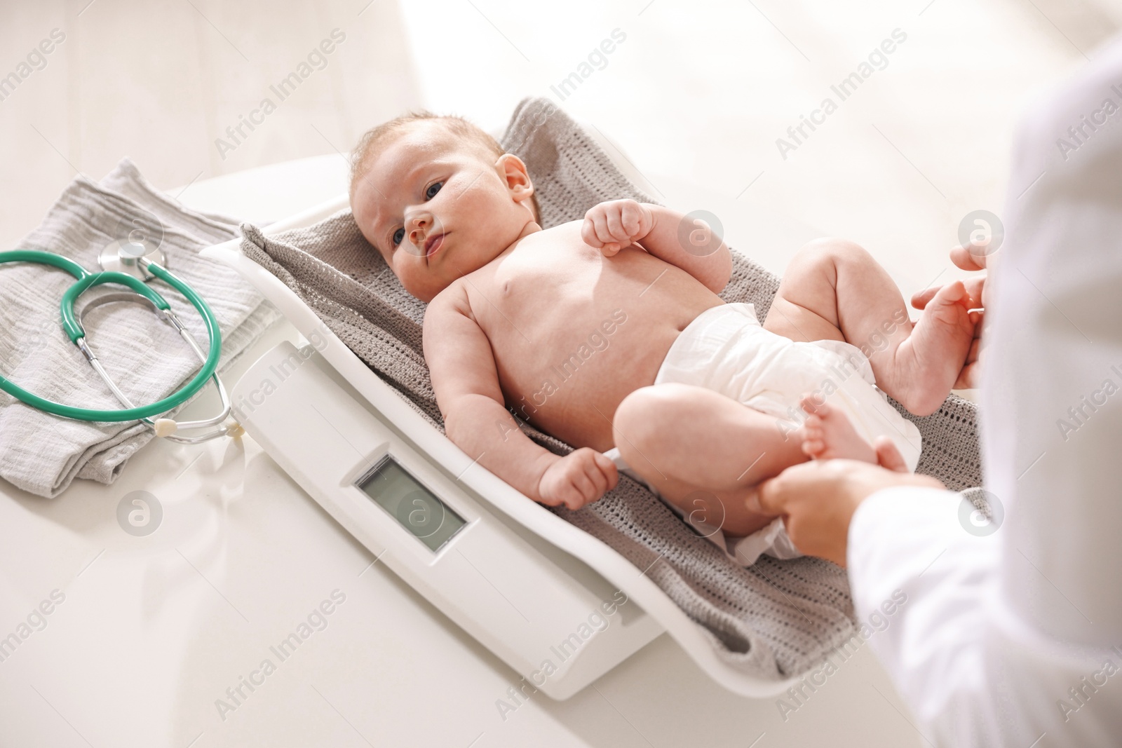 Pediatrician weighting baby with scales at white table in clinic, closeup Photo of Pediatrician weighting baby with scales at white table in clinic, closeup