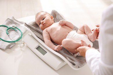 Photo of Pediatrician weighting baby with scales at white table in clinic, closeup