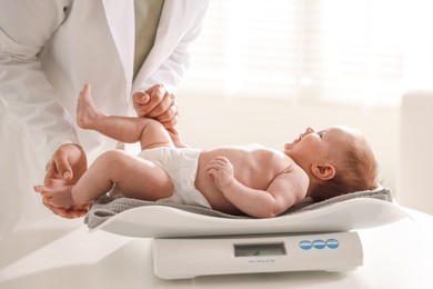 Photo of Pediatrician weighting baby with scales at white table in clinic, closeup