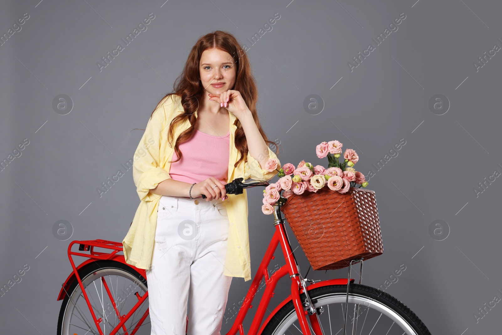 Beautiful teenage girl and bicycle with basket of flowers against grey background Photo of Beautiful teenage girl and bicycle with basket of flowers against grey background