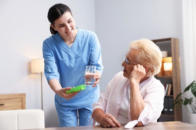 Photo of Nurse giving glass of water and pills to senior woman indoors. Home health care service