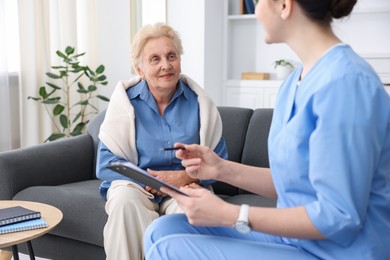 Photo of Nurse with clipboard examining senior woman indoors, closeup. Home health care service