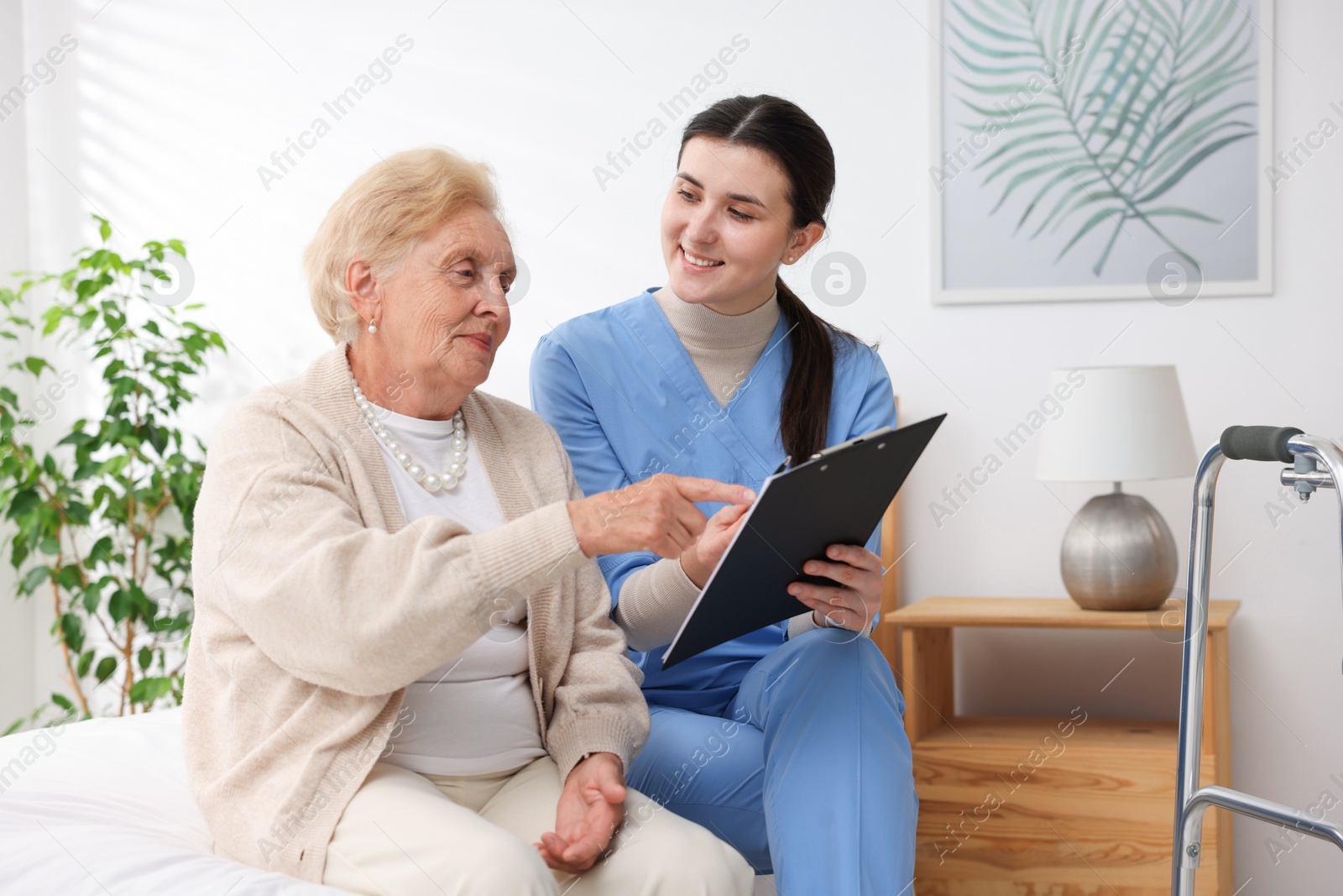 Nurse with clipboard examining senior woman indoors. Home health care service Photo of Nurse with clipboard examining senior woman indoors. Home health care service