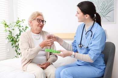 Photo of Nurse giving pills and glass of water to senior woman indoors. Home health care service