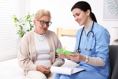 Photo of Nurse giving pills to senior woman indoors. Home health care service
